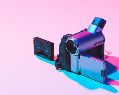 close up view of video cassette and digital video camera on pink background